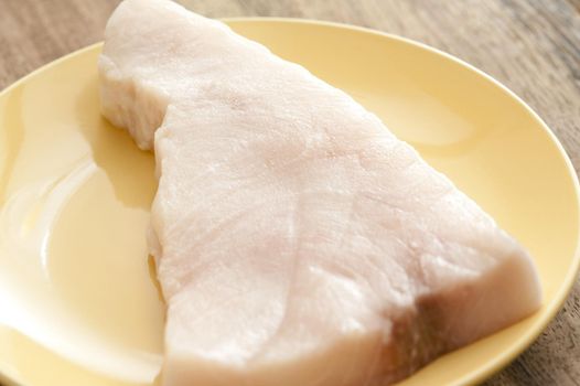 Close up of on chunky cut of swordfish in round yellow plate placed on rustic wooden table
