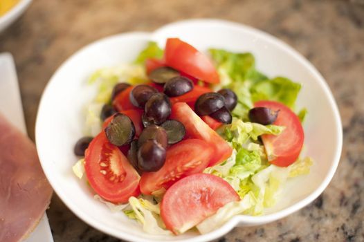 White ceramic bowl with green salad, grapes and tomatoes, high-angle close-up