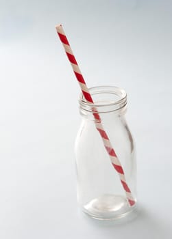 Empty kids glass milk bottle with striped red and white plastic straw over a white background with copy space