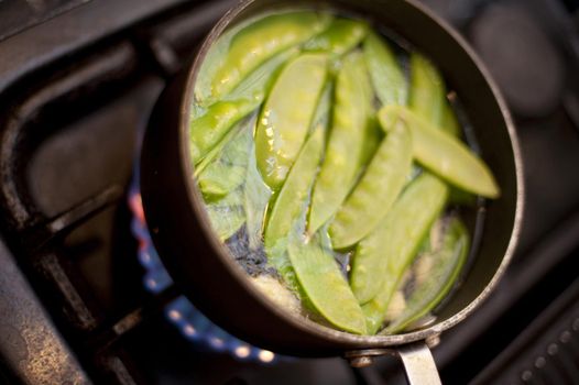 Mangetout peas boiling in a pot on a gas stove for a delicious accompaniment to a meal or vegetarian and vegan cuisine