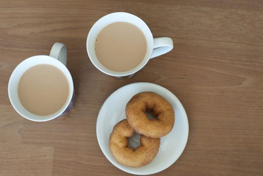 Aerial View of Cups of Creamy Coffee and Plate of Doughnuts on Side Served on Brown Wooden Table