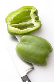 Two halves of green pepper lying on knife against of white background. From above