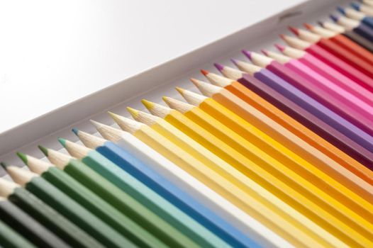 Open box of newly sharpened pencils in dark and bright colors arranged in a long row with selective focus