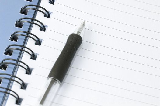 Spiral bound blank lined notebook page with a plastic ballpoint pen with room for your text or message