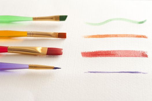 Series of paint strokes from different colorful plastic brushes with assorted shapes and widths of bristles painted on white paper, low angle view in a line