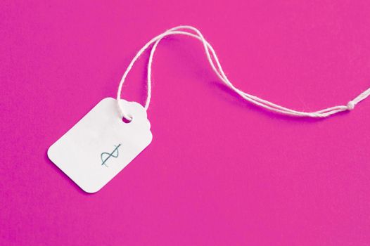 White cardboard price label or tag with string and a handwritten dollar sign lying on a bright pink background with copy space