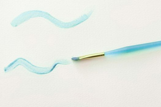 High Angle Still Life of Plastic Child Paintbrush Painting Squiggly Lines in Blue Paint on White Paper Background with Copy Space