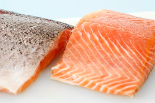 Close up view of two fresh uncooked salmon steaks on a plate, one facing down to reveal the skin