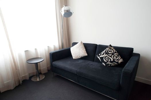 Modern living room decor in stylish black and white with a comfortable sofa, side tables and standard lamp alongside a floor height window