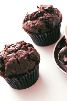Tilted angle view on two freshly baked chocolate muffins on white table with subtle set down shadow