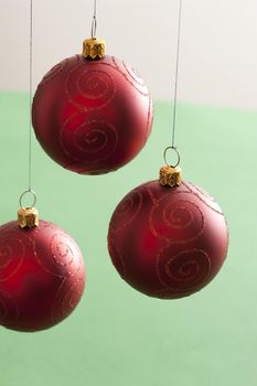Three hanging red Christmas baubles with glitter decoration over a bicolour green and white background