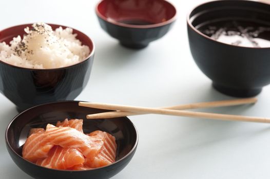Raw salmon sashimi pieces served with rice and a soy dipping sauce in traditional individual bowls for gourmet Asian cuisine