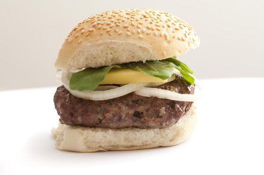 Fat homemade oddly shaped hamburger patty on a seeded bun with onion slices, cheese and lettuce leaves