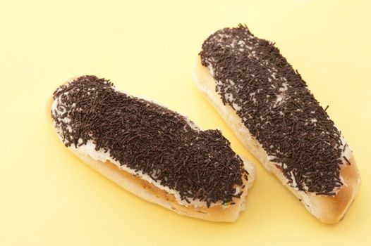 two chocolate sprinkle covered sticky buns on a yelllow background