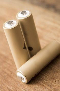 Three natural coloured AA rechargeable cell batteries isolated on a brown timber background.