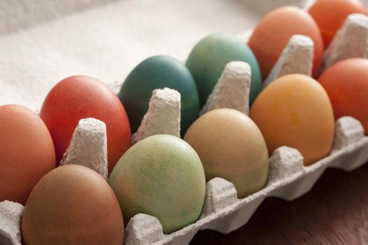 Close up view of opened paper egg box with colorful dyed Easter eggs on wooden table