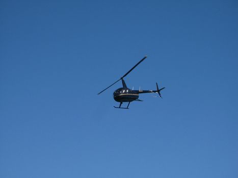 Black Helicopter Flying up in the Blue Gray Sky, Emphasizing Copy Space.