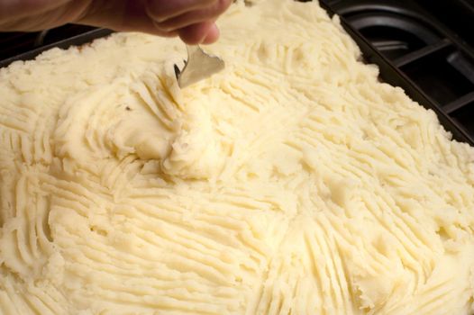 Cottage pie preparation with a cook smoothing the mashed potato crust over the meat with a fork before baking or grilling