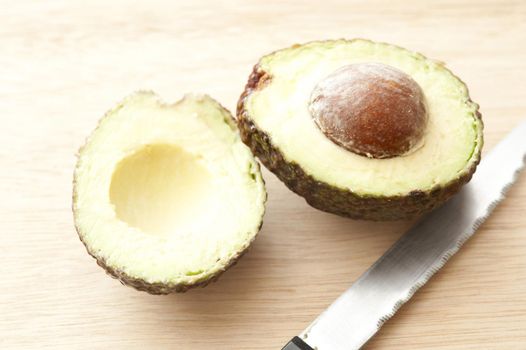 Fresh cut avocado with seed and knife on wooden table