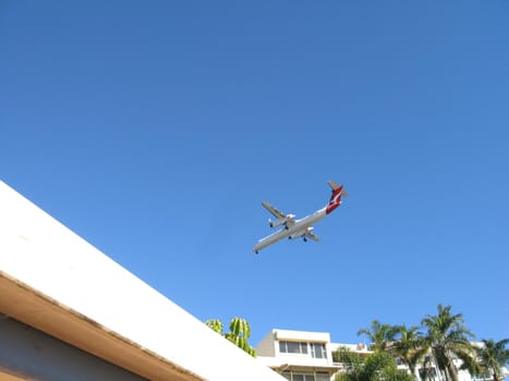 Aircraft coming on to land over the tops of whitewashed houses in a tropical resort conceptual of travel and summer vacations