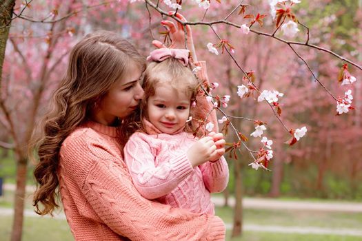 mother and little girl in pink clothes, hugging in the park with blooming pink sakura. Close up