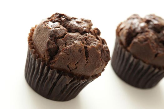Two homemade delicious chocolate chip muffins with brown cupcake wrapper, oblique close up with copy space