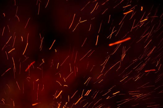 Background of fiery trails from glowing embers shooting through the darkness from a burning bonfire