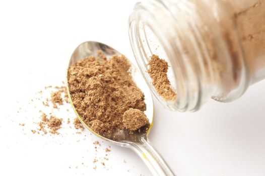 Spoonful of dried ground coriander powder in a silver teaspoon below the open spice bottle over a white background with copy space