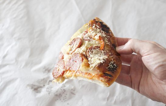 Man holding the last slice of salami or pepperoni pizza topped with spicy sausage, cheese and onion over crumpled white paper