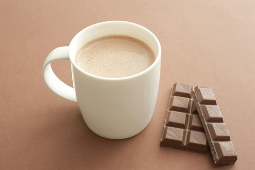White mug of cacao and milk chocolate on brown background.