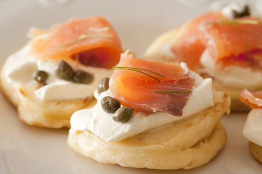 Close up view on delicious capers and raw fish blini appetizers showing smooth texture and little herb topping