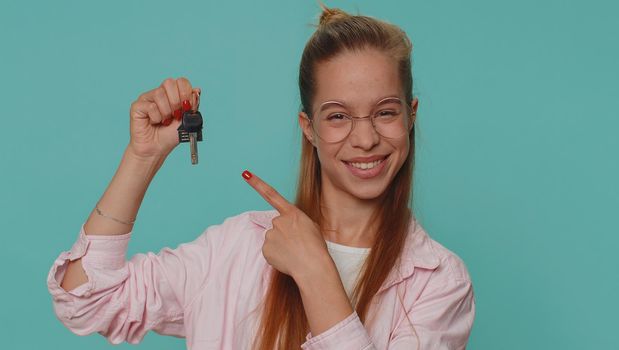 Teenager young girl real estate agent lifting hand showing the keys of new home house apartment, buying or renting property, mortgage loan. Student child kid isolated on blue studio background indoors