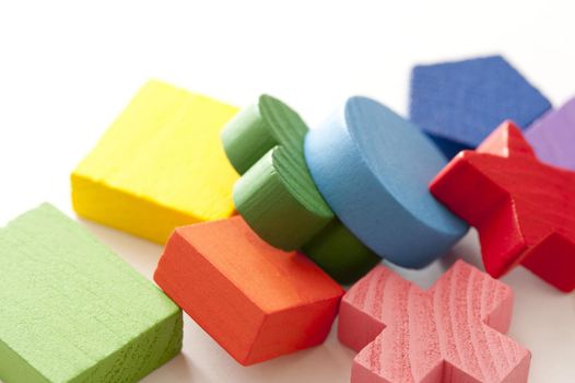 Colorful educational wooden toy blocks in a variety of different basic geometrical shapes lying in a heap on white