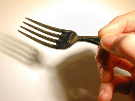 Close up of the fingers of a man holding a fork casting a shadow onto a white plate