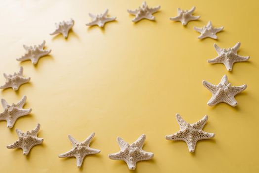 Circle of clean white dried starfish on a yellow background with copy space for your marine, nautical or summer vacation themes