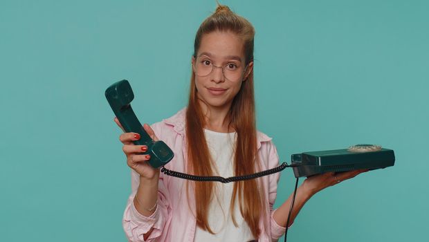 Hey you, call me back. Pretty teenager girl child kid talking on wired vintage telephone of 80s, says hey you call me back. Young stylish female student isolated on blue studio background indoor