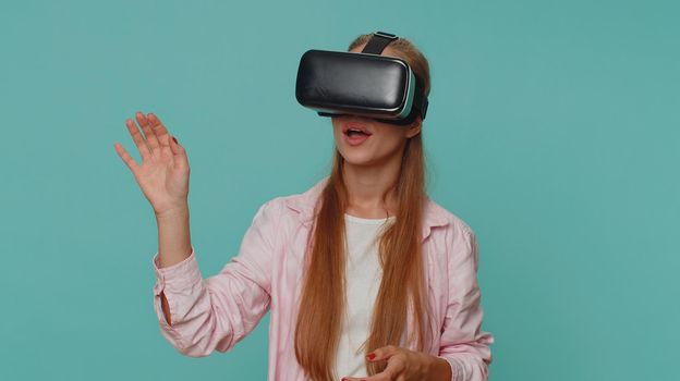 Excited teenager young girl using headset helmet app to play simulation game. Watching virtual reality 3D 360 video. Student child kid in VR goggles device isolated on blue studio background indoors
