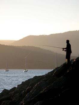a man fishing at sunset from a marina wall