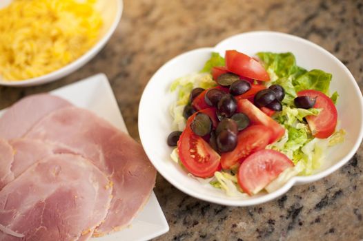 Cold lunch of fresh mixed salad with lettuce, tomato and olives served with a plate of sliced cured ham