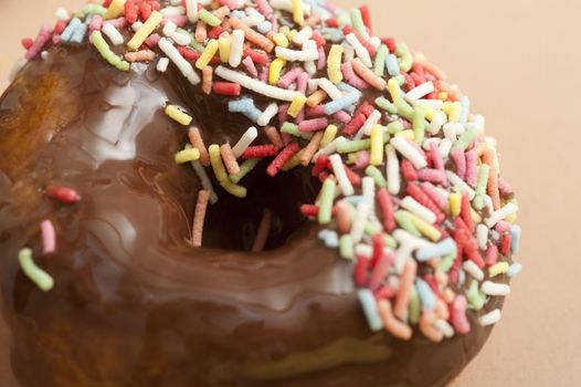 Chocolate glazed donut or doughnut dipped in multicolored sprinkles for a tasty tea or coffee break snack, closeup view