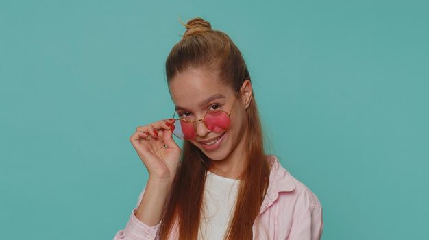 Portrait of seductive pretty teenager child kid wearing sunglasses, charming smile. Young stylish female teen student girl isolated alone on blue studio background indoors. People emotions concept