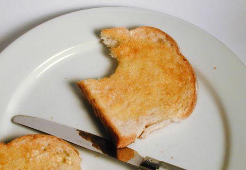 Slice of hot buttered white toast on a white plate for breakfast bitten into on the corner