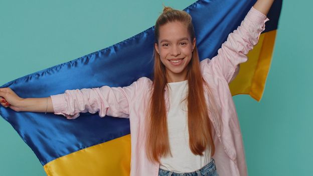 Teen young girl hold Ukraine national flag hoping for success, smiling with kind optimistic expression. Independence, freedom, victory in war, national holiday. Student child kid on blue background