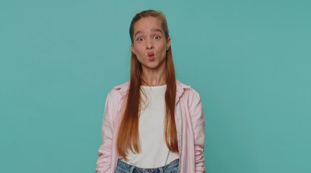 Lovely pretty funny girl in shirt making playful silly facial expressions and grimacing, fooling around, fish face. Young stylish female child kid isolated alone on blue studio background indoors