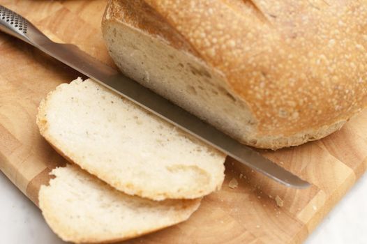 Delicious freshly baked crusty loaf with sliced bread and a bread knife on a wooden board, close up high angle view