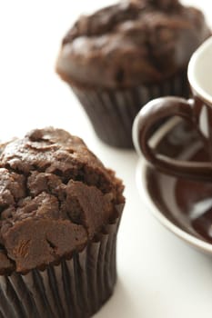 Pair of freshly baked large chocolate muffin desserts beside brown coffee cup and saucer