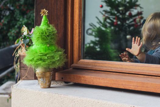 Little girl with a palm on the glass looking at the Christmas tree