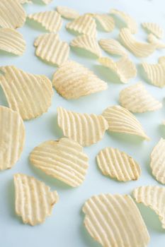 Background of scattered crinkle cut potato crisps on a light green background viewed high angle for a tasty but unhealthy snack
