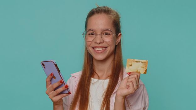 Happy teenager girl use smartphone, plastic credit bank card, browsing say wow yes, found out great big win, success lotter, good news, purchases online shopping. Child kid on blue studio background