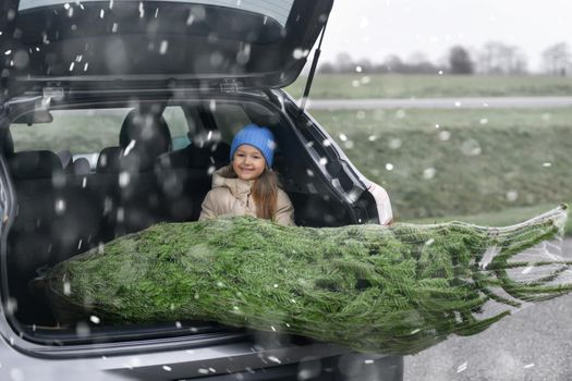 A girl sitting in the trunk with a Christmas tree